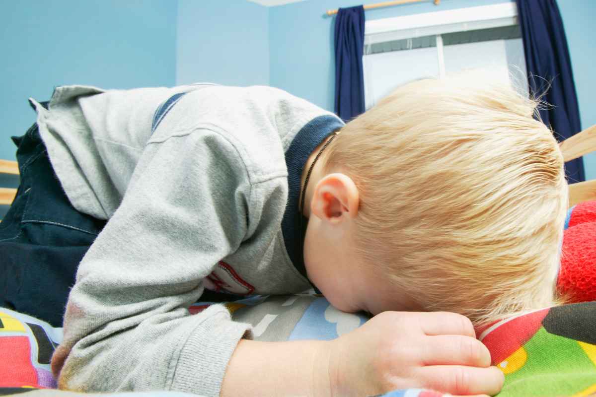 Bambino biondo che piange sul letto